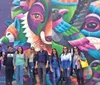 A group of people are standing in front of a colorful mural featuring stylized animal faces