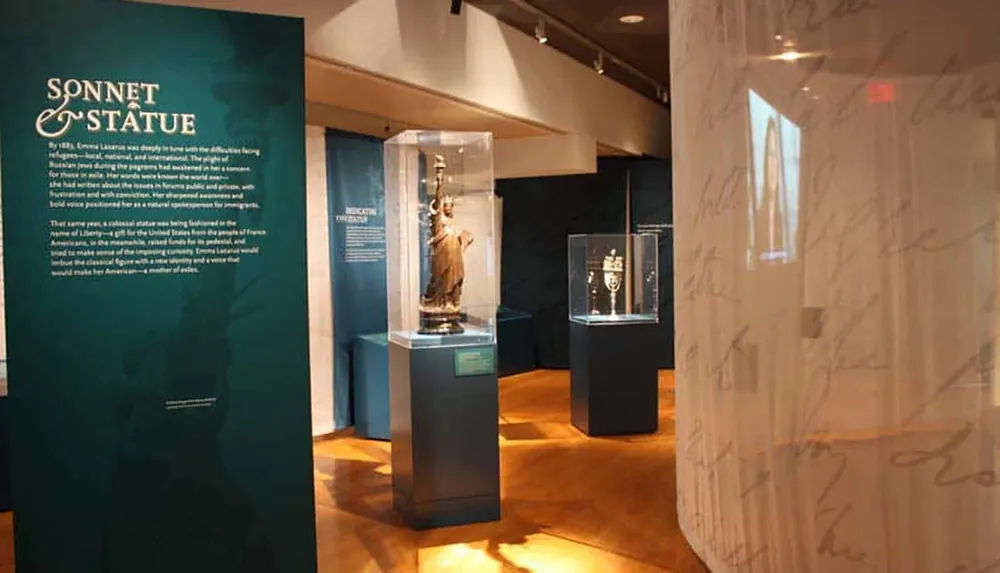 The image depicts an exhibition space with information panels and display cases containing models or replicas of the Statue of Liberty and other artifacts focusing on the theme Sonnet  Statue
