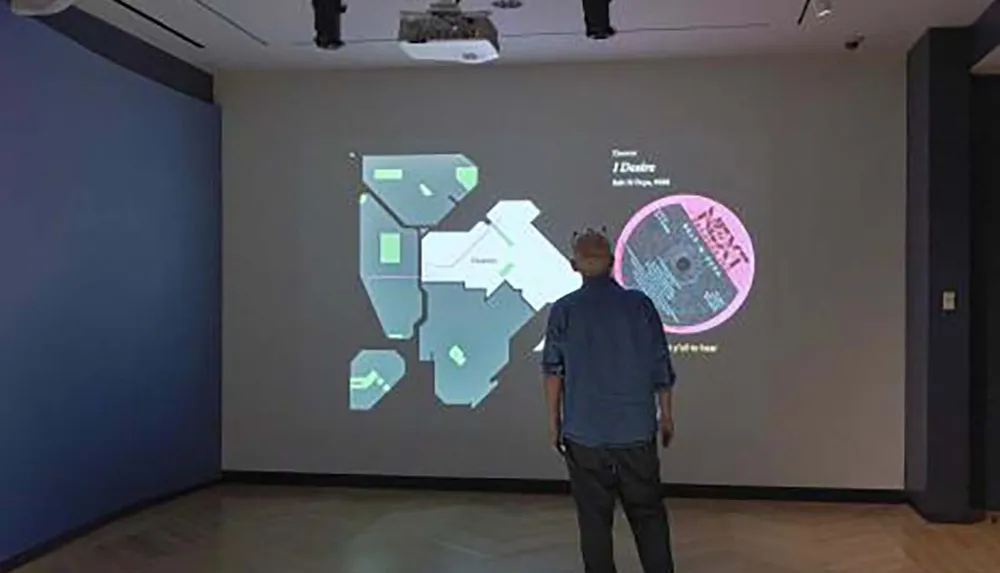 A person is observing a projected interactive display featuring abstract shapes and texts on a wall