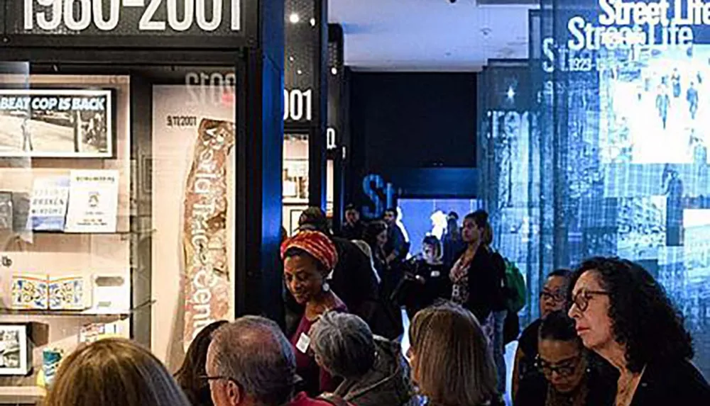 The image shows a group of people inside a gallery or museum looking at various displays and engaging with an exhibition