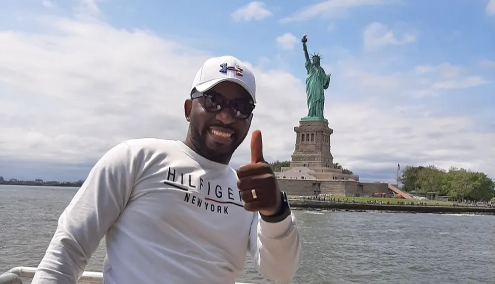 A person is giving a thumbs-up with the Statue of Liberty in the background