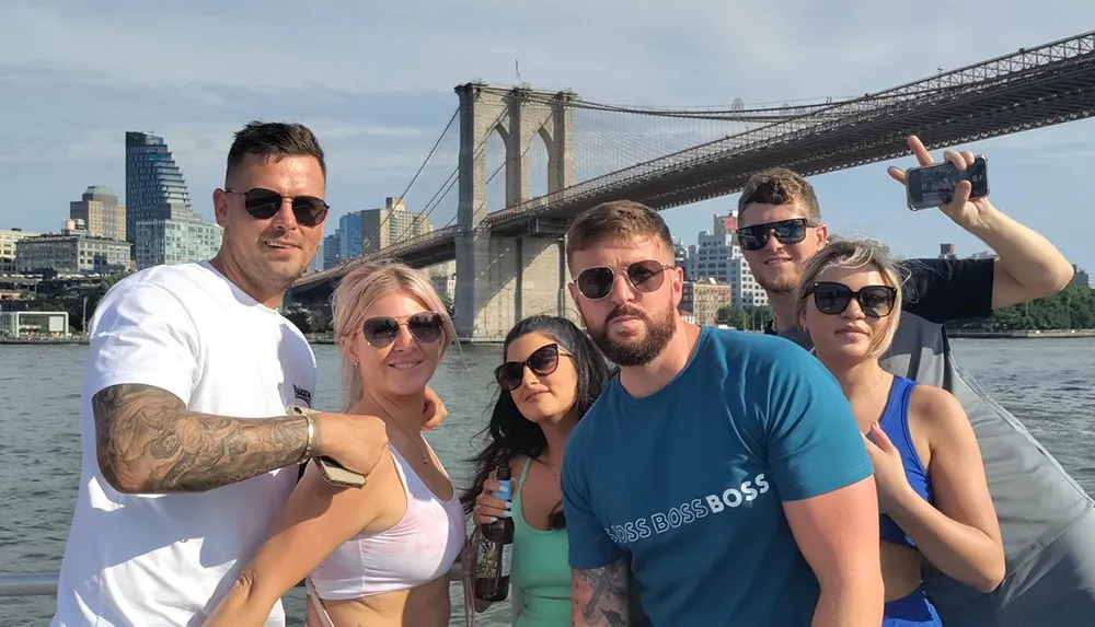 A group of friends pose for a photo with the Brooklyn Bridge in the background while enjoying a boat trip