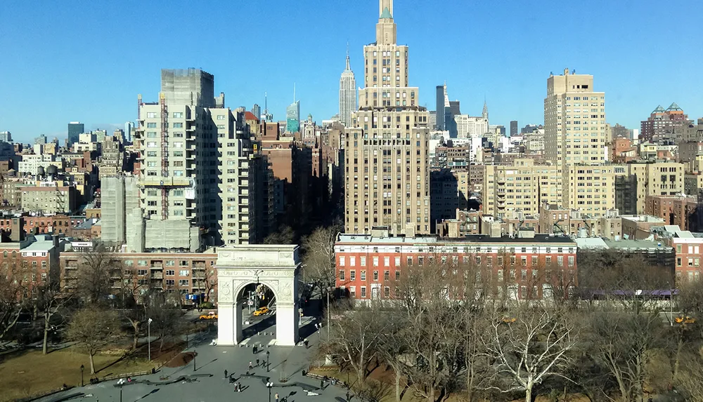 The image features a sunny aerial view of Washington Square Park with its iconic arch surrounded by the diverse architecture of New York City buildings including the Empire State Building in the distance