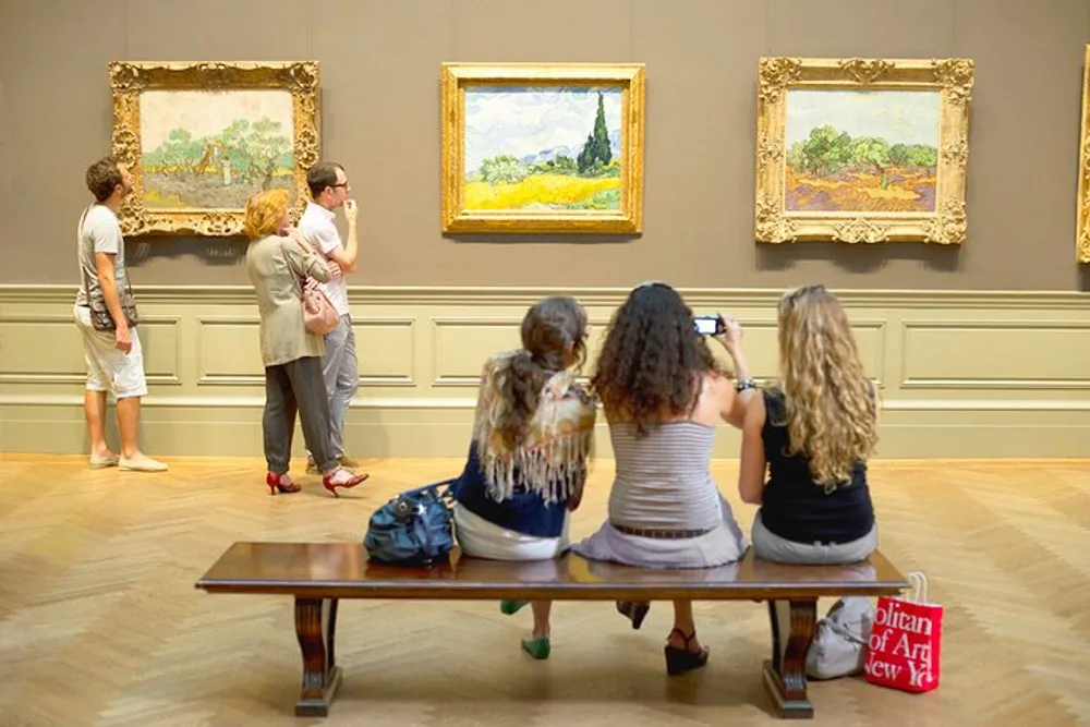 Visitors are viewing and photographing paintings on display in an art gallery