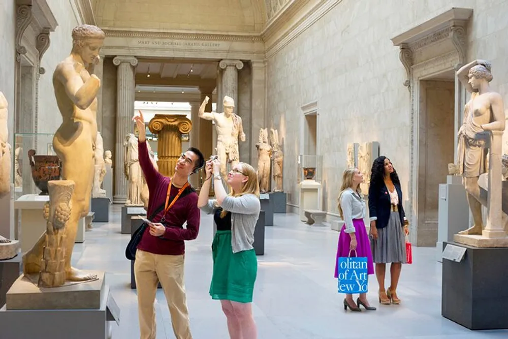 A group of visitors is engaged in observing and photographing classical statues in a bright spacious museum gallery