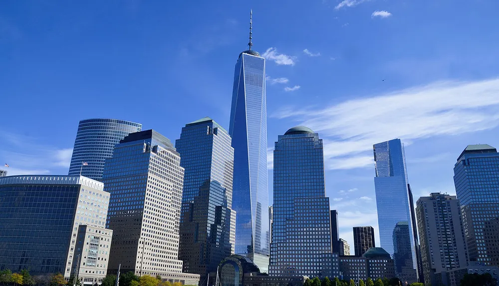 The image shows the Lower Manhattan skyline with One World Trade Center standing tall against a clear blue sky