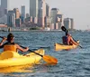 A man and a woman are kayaking in front of an urban skyline