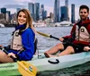 A man and a woman are kayaking in front of an urban skyline