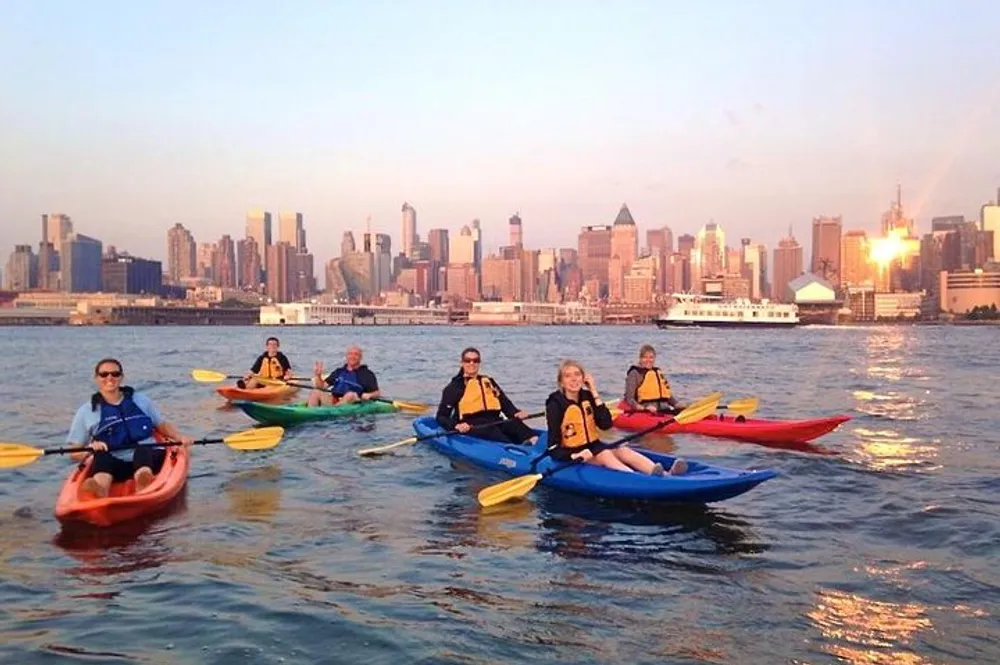 A group of kayakers enjoys an outing on the water with a view of a city skyline at sunset