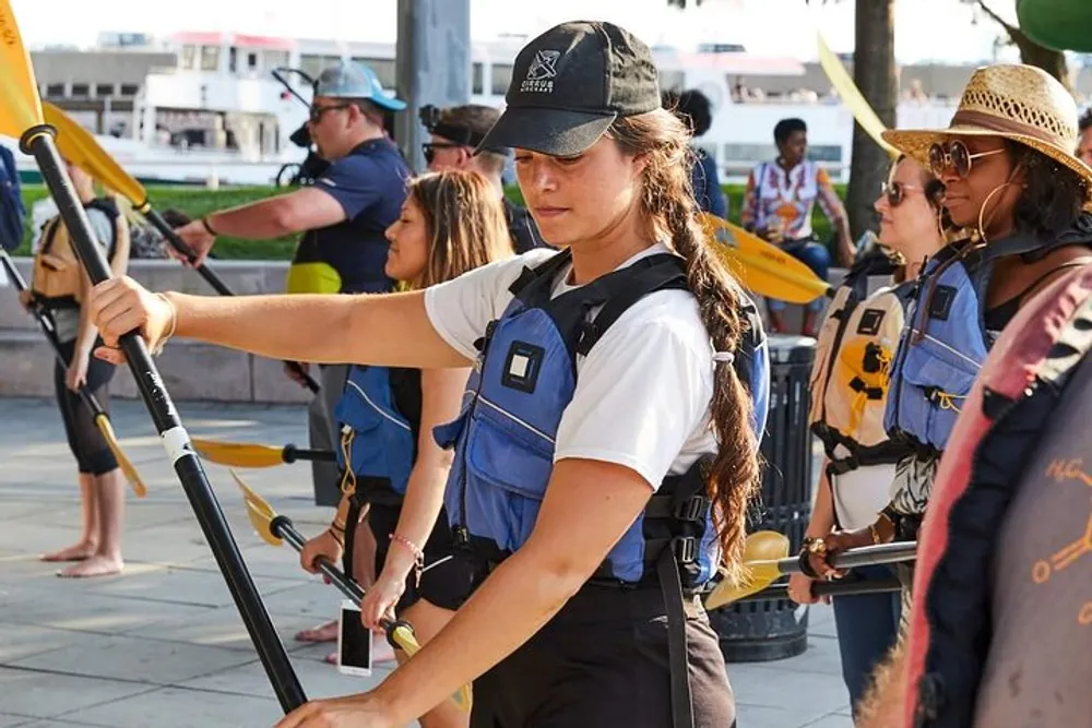 A group of people wearing life vests and holding paddles seems prepared for a water activity with a focused individual in the foreground