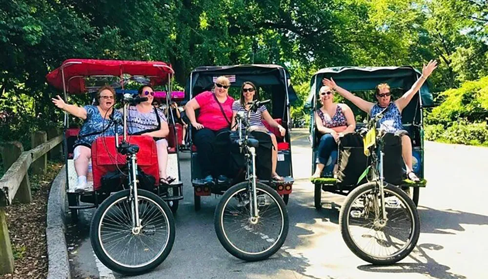 A group of women appear to be enjoying themselves while riding in multi-passenger pedicabs with two individuals playfully posing on penny-farthing bicycles in the foreground