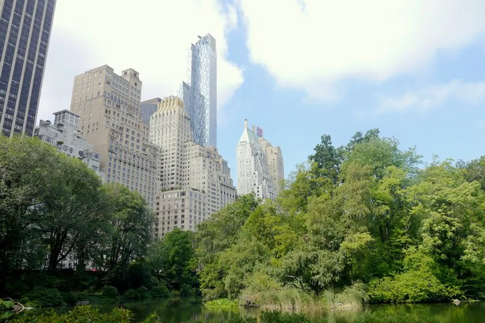 A serene park with lush greenery in the foreground contrasts with the towering skyscrapers in the background under a partly cloudy sky