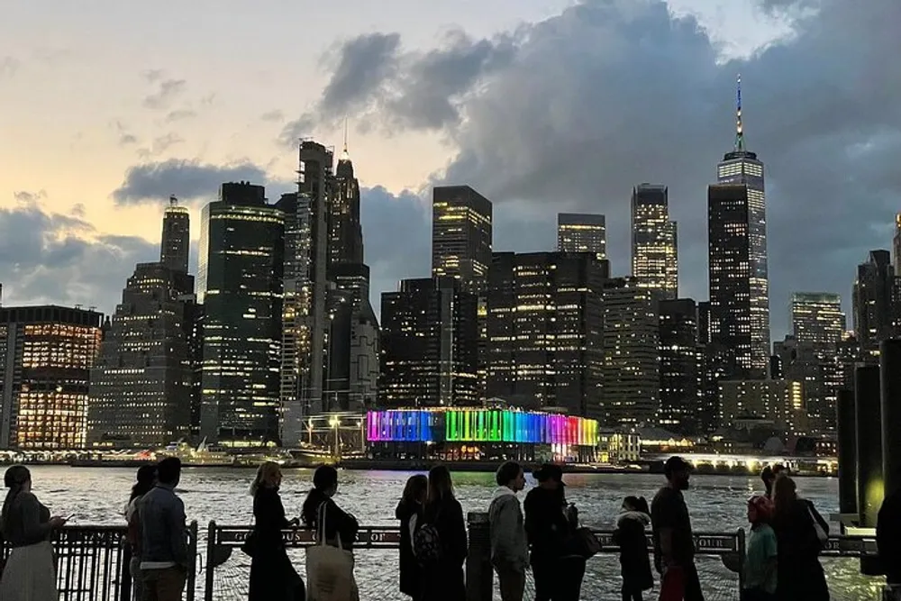 People are observing a vibrant illuminated skyline across the water during dusk