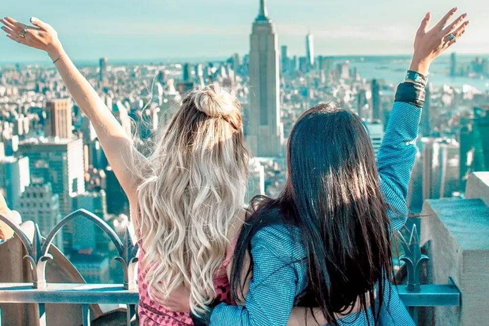 Two people are enjoying a scenic view of a city skyline with their arms raised in a gesture of excitement or freedom