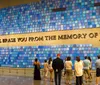 The image shows two preserved columns from a damaged structure displayed in a modern space with a glass ceiling beneath which hangs a row of colorful firefighter helmets