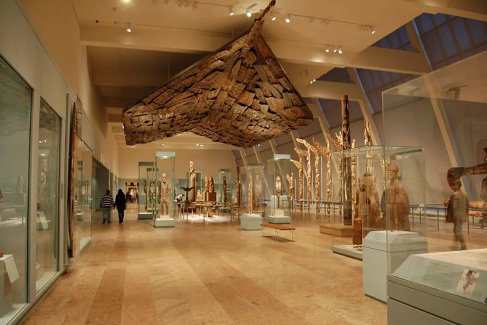 Visitors explore an exhibit featuring a suspended wooden canoe and various cultural artifacts inside a spacious museum gallery