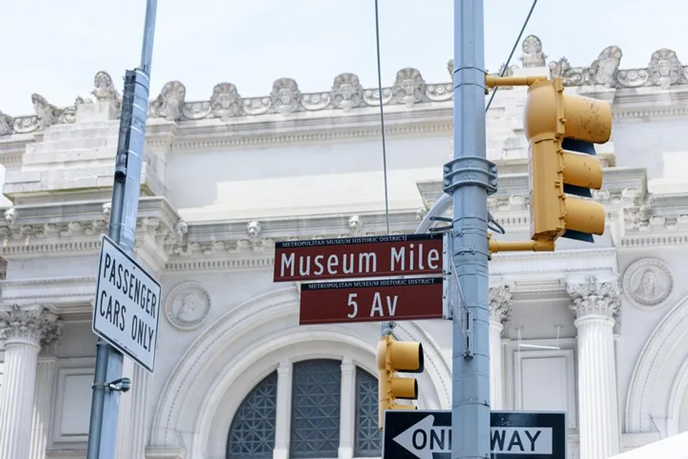 The image features street signs including one indicating Museum Mile on 5th Avenue with yellow traffic lights and a classical building facade in the background