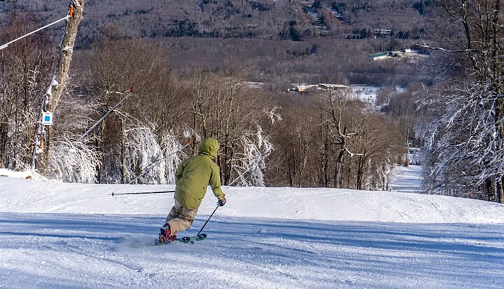 A person is skiing down a snow-covered slope with a ski lift and trees in the background