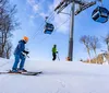 Two skiers are descending a snowy slope with a ski lift operating in the background under a clear blue sky