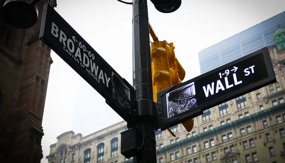 A street sign intersection for Broadway and Wall Street with an image of a charging bull symbolizing the financial markets located in Lower Manhattan New York City