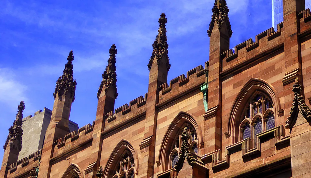 The image shows the ornate Gothic architecture of a building with pointed arches and spires against a clear blue sky