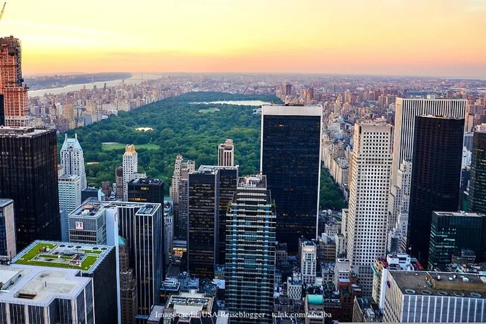 The image captures a breathtaking aerial view of Central Park in New York City surrounded by a dense arrangement of skyscrapers and buildings at sunset