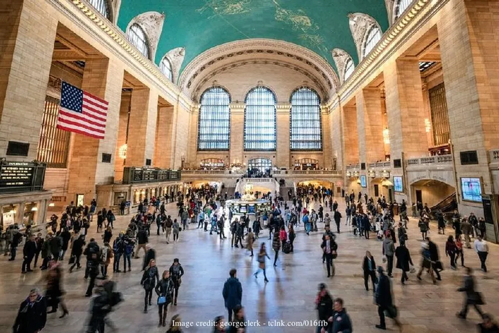 The image shows the bustling interior of a grand train station with high arched windows an American flag and a ceiling decorated with celestial motifs