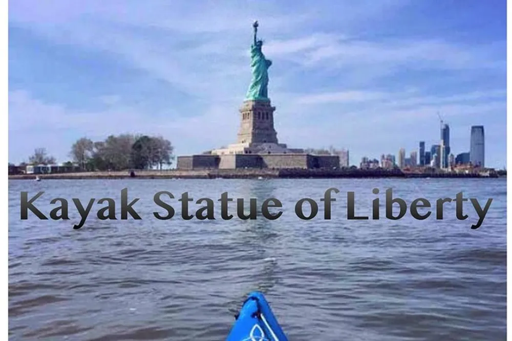 The image shows the view from a kayak on the water near the Statue of Liberty with the New York City skyline in the background