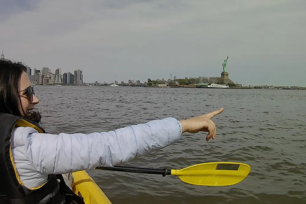 A person is kayaking near the Statue of Liberty with a view of a city skyline in the background