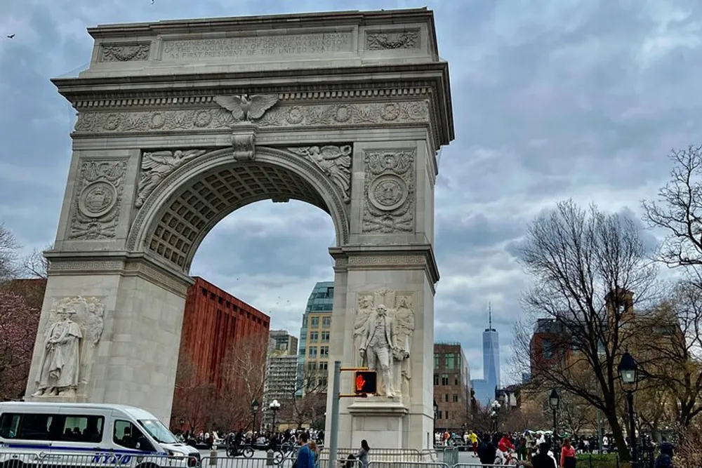 The image depicts the Washington Square Arch with a bustling crowd and a view of the Freedom Tower in the background under a cloud-filled sky