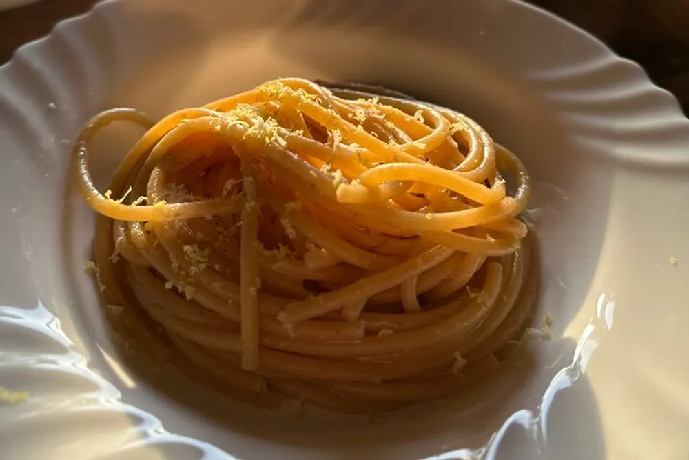 The image shows a neatly twirled portion of spaghetti topped with grated cheese illuminated by warm light on a white plate