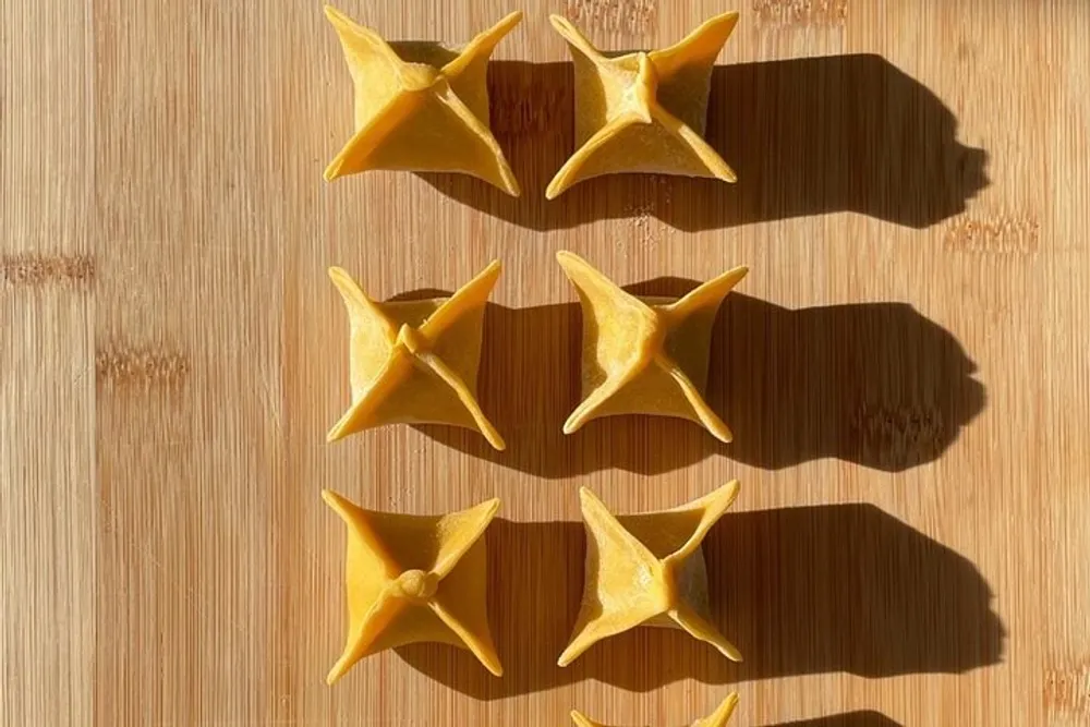 Six pointed star-shaped pasta pieces are neatly arranged on a wooden surface bathed in sunlight casting prominent shadows