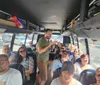 A group of passengers is listening to a man who seems to be speaking or guiding them as they sit inside a bus