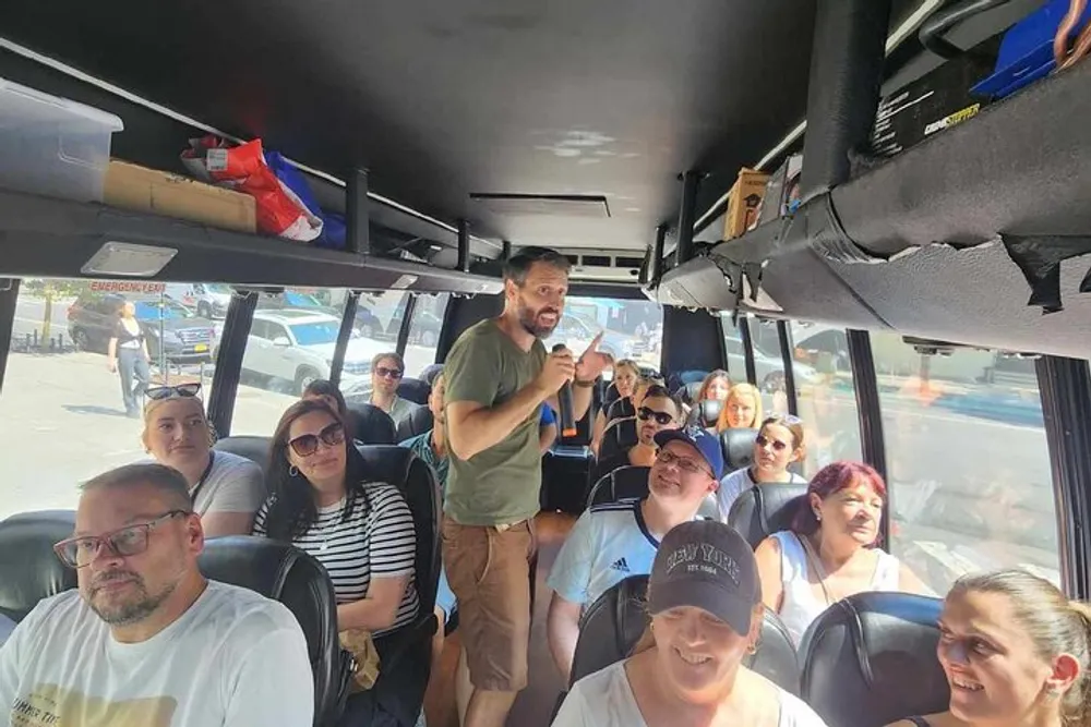 A group of passengers is listening to a man who seems to be speaking or guiding them as they sit inside a bus