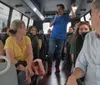 A group of passengers is listening to a man who seems to be speaking or guiding them as they sit inside a bus