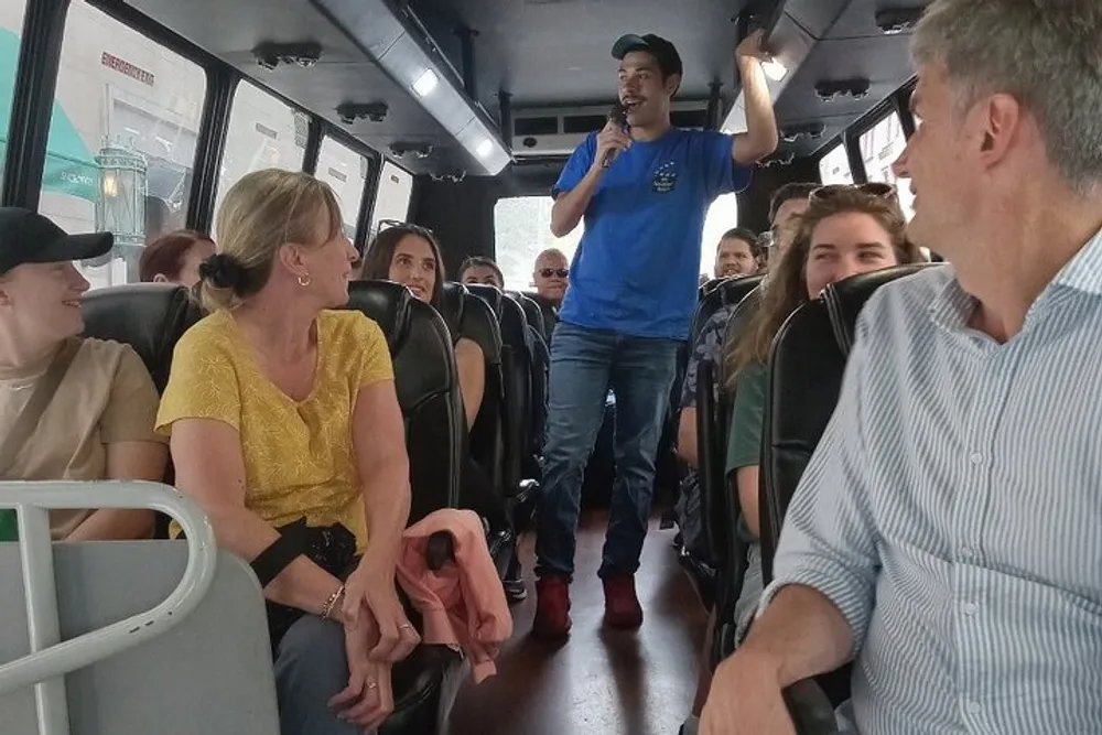 A tour guide is speaking to a group of attentive passengers on a bus