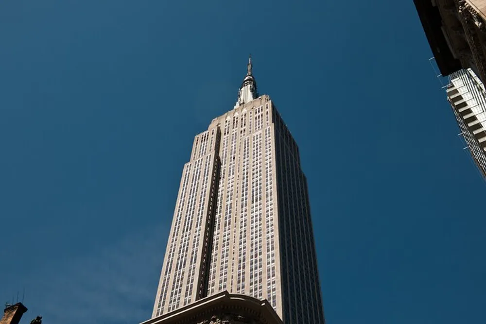 The image showcases a towering skyscraper extending into a clear blue sky viewed from a street-level perspective