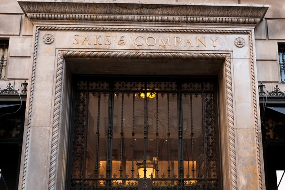 The image shows the ornate entrance of the Saks  Company building with intricate metalwork and a lit interior visible through the gate