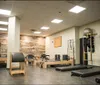 A person is stretching on the floor of a gym with weights in the background bathed in natural light coming through large windows