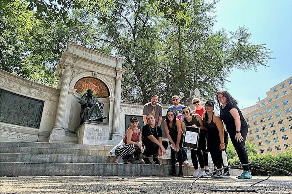 A group of people pose for a photo in front of a monument with a seated bronze figure under a sunny sky