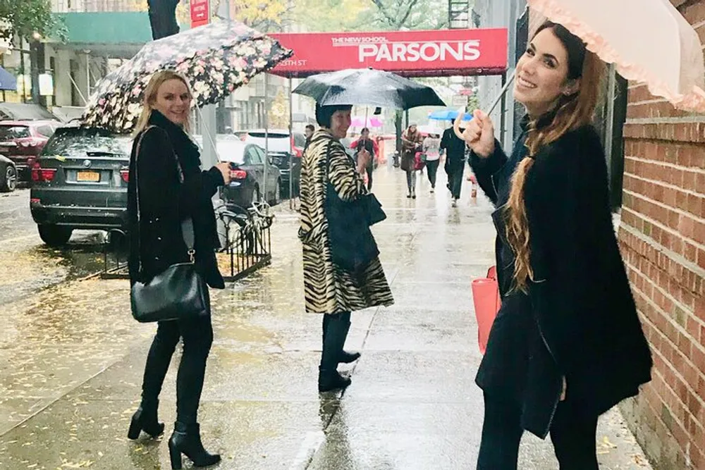 Three individuals with umbrellas are walking on a wet city sidewalk on a rainy day