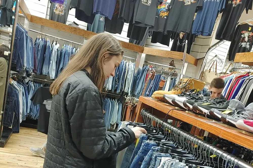 A person is browsing through clothing at a retail store with a focus on jeans and casual wear