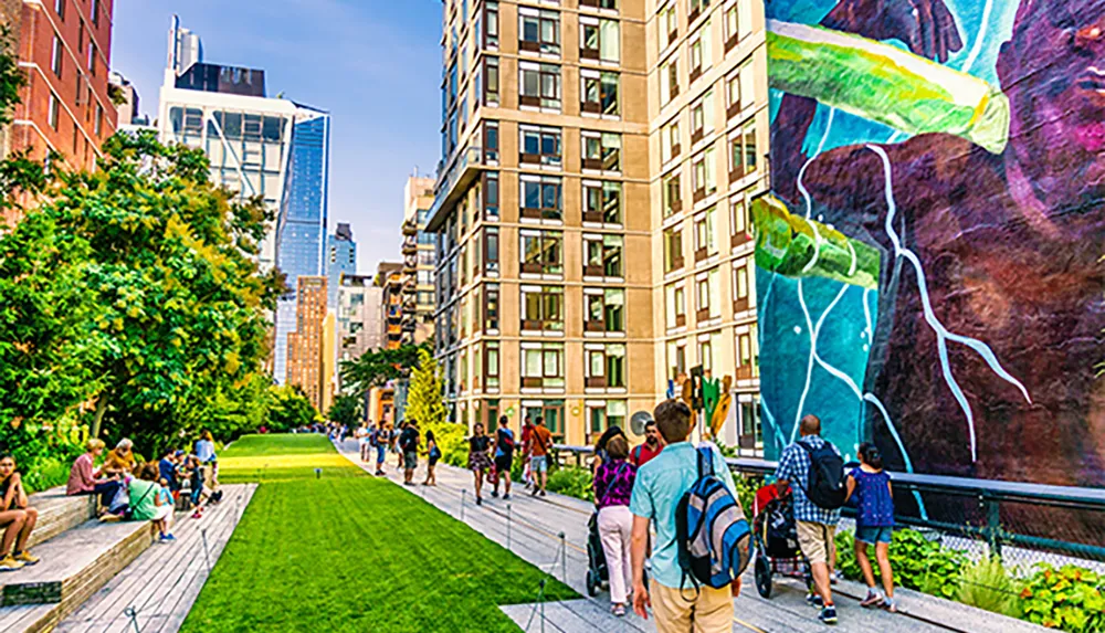 People walk along an urban park with vibrant greenery and a large colorful mural on the building to the right encapsulating a blend of nature art and city life