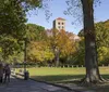 A couple walks hand in hand along a tree-lined pathway in a park during autumn with a historical tower building in the background