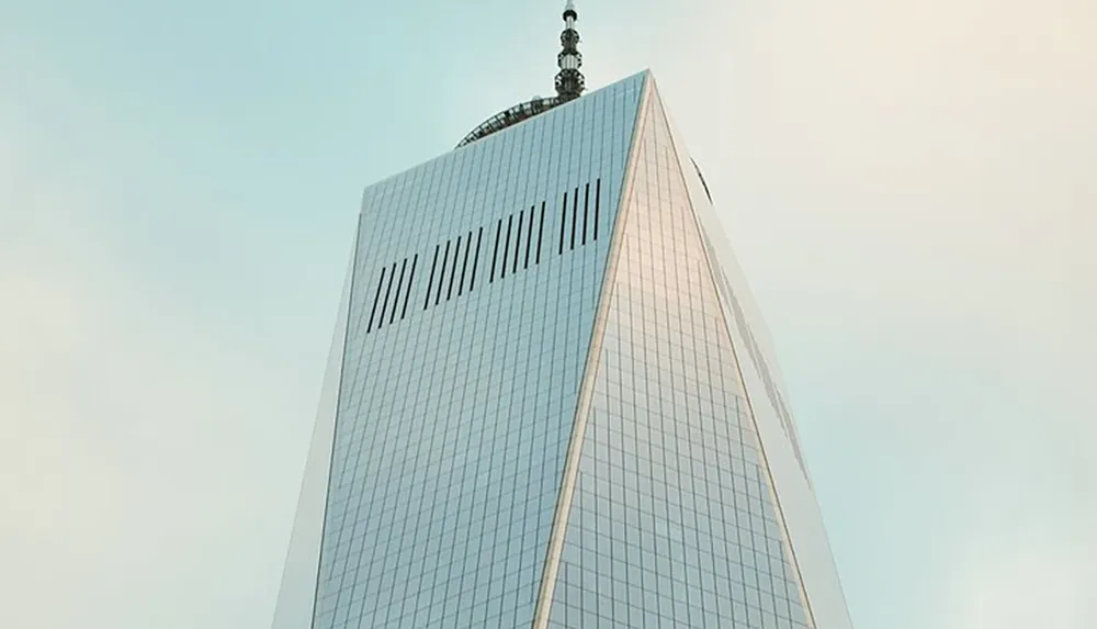 The image shows the upper part of a modern glass skyscraper against a clear sky with its rooftop spire adding to its impressive height