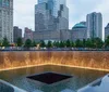 This image shows a memorial reflecting pool surrounded by trees and skyscrapers in an urban setting at twilight