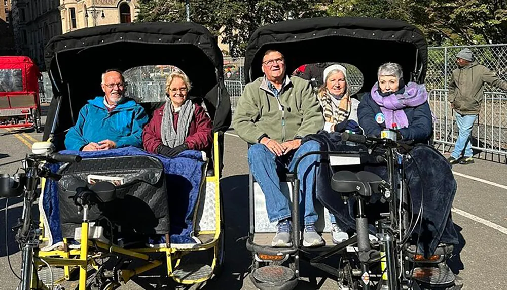 The image shows four smiling adults seated in two pedal-powered rickshaws enjoying a sunny day outdoors