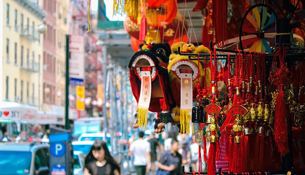 The image captures a vibrant street scene with a focus on colorful Chinese decorations and cultural items for sale with pedestrians and urban life in the background