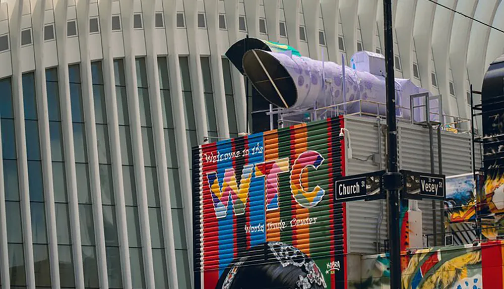 The image shows an urban scene with colorful artwork on a building a sign reading Welcome to the WTC and street signs for Church St and Vesey St against the backdrop of the smooth paneled exterior of a modern building