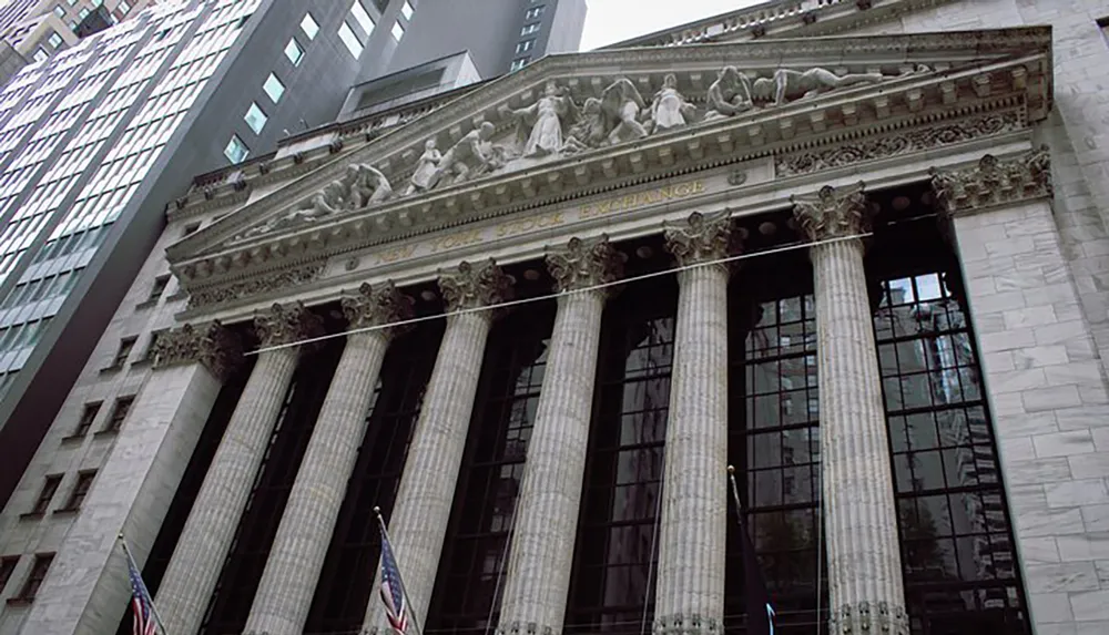 The image shows the neoclassical facade of the New York Stock Exchange with its iconic Corinthian columns and sculpture above the entrance